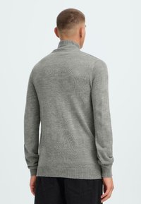 Grå strikket genser med høy krage, lange ermer og ribbestrikkede mansjetter og nederkant. Myk tekstur og tettsittende design.