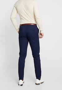 Granatowe spodnie z teksturowanej tkaniny o dopasowanym kroju, z dwoma tylnymi kieszeniami i brązowym skórzanym paskiem. Całość dopełniają białe trampki.