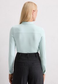 Vaaleansininen pitkähiha Shirt, jossa on kaulus ja nappikoristeet hihansuissa, yhdistettynä tummanharmaisiin korkeavyötäröisiin housuihin, joissa on takataskut.