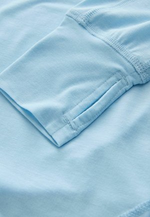 Gaiši zils kokvilnas audums ar mīkstu tekstūru, ar salocītu piedurkni un kārtīgi šūtiem šuvēm, ar smalku spīdumu.