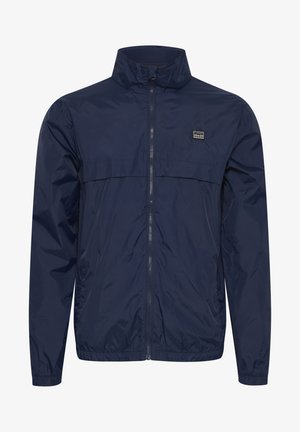 Navy windbreaker jacket featuring a high collar, front zipper, and chest logo patch; made from lightweight, textured fabric.