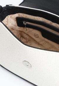 Borsa in tela e pelle con rifiniture nere e corpo bianco. L'interno presenta un rivestimento beige con una tasca con zip e un motivo con logo. Chiusura magnetica.