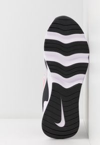 Semelle de chaussure de sport noire et blanche avec des rainures ondulées ; accent rose sur le côté. Caoutchouc lisse avec grip texturé. Logo Nike sur le talon.