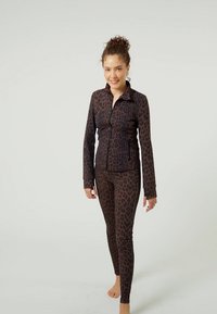 Smeđa jakna na patentni zatvarač s uzorkom leoparda u kombinaciji s odgovarajućim tajicama. Glavne značajke su rastezljivi materijal, uski kroj, dugi rukavi i ovratnik.