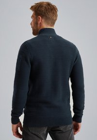 Gebreide donkerblauwe trui met een hoge kraag, geribbelde manchetten en onderkant, met een gestructureerd patroon en een klein logo detail op de achterkant.