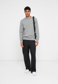 Felpa grigia con polsini e orlo ribattuti, abbinata a pantaloni cargo neri con molteplici tasche e sneakers bianche. Design semplice.