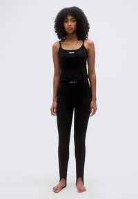 Débardeur noir sans manches avec un logo blanc, associé à un legging noir avec une bande logo à la taille. Texture lisse, coupe ajustée.