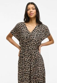 Robe à imprimé léopard avec décolleté en V, manches courtes et taille cintrée. Fabriquée en tissu léger avec une texture fluide et douce.