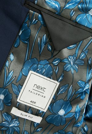 Lieknas švarkas tamsiai mėlynos spalvos audinyje, turintis gėlių rašto pamušalą mėlynos ir pilkos atspalvių, su prekės ženklo baltu etikete.