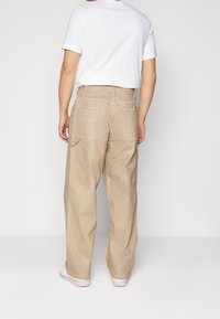 Ljust beigefärgade cargo-byxor med lös passform, flera fickor på sidorna och baksidan, samt kontrasterande vit sömnad. Matchat med en vit t-shirt.