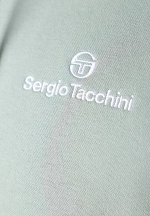 Groene stof met een gladde textuur heeft witte geborduurde tekst "Sergio Tacchini" en een cirkelvormig logo.