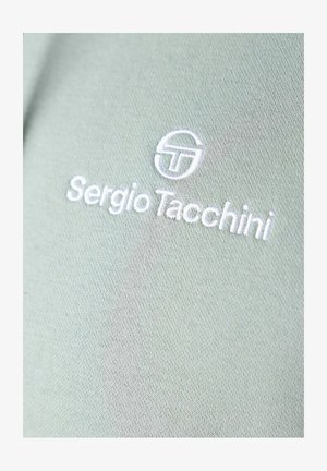 Groene stof met een gladde textuur heeft witte geborduurde tekst "Sergio Tacchini" en een cirkelvormig logo.