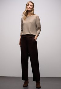 Beiger Strickpullover mit weitem Ausschnitt und gerippten Bündchen, kombiniert mit dunkelbraunen, hoch taillierten Hosen mit Seitentaschen und Knopfdetail.