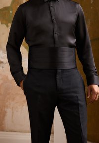 Black dress shirt with a glossy finish, featuring a wide satin waist accent, paired with textured black trousers, subtly patterned.