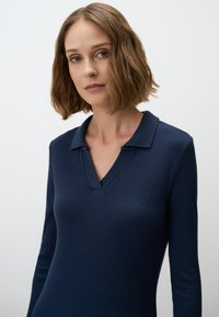 Marineblauer, gerippter Langarm-Pullover mit V-Ausschnitt und klassischem Kragen. Glatte Textur mit taillierter Silhouette, die ein elegantes Design betont.