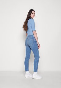 Top justo azul claro combinado com jeans azuis de corte slim e cintura alta. O modelo usa ténis brancos e meias brancas até ao joelho.