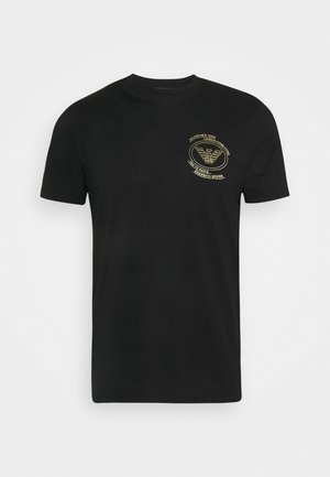 Czarny t-shirt z krótkim rękawem i okrągłym dekoltem, z małym złotym emblemą po lewej stronie klatki piersiowej, przedstawiającym stylizowanego orła oraz nazwy miast w okrągłym wzorze.