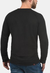 Black long-sleeve shirt with a textured finish and raglan sleeves, featuring a round neckline and a small logo accent near the hem.