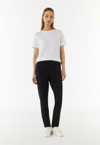Witte korte mouwen t-shirt met opgerolde mouwen, gecombineerd met zwarte tapered broek en witte sneakers. Simpel ontwerp, zachte stof, casual uitstraling.