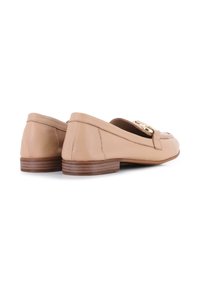 Mocasines de cuero beige con un bajo tacón de madera y un acento decorativo de hardware dorado en el empeine. Textura suave y diseño de punta redondeada.