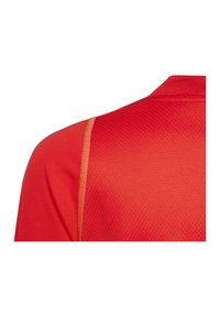 Rode sporttrui met textuurstof, een polokraag en contrasterende oranje naden langs de schouder.