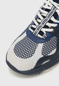 Sportowe buty w kolorze granatowym i białym, z siateczkową cholewką, gładkimi skórzanymi akcentami, wytrzymałymi sznurowadłami, teksturowaną podeszwą oraz zaokrąglonym noskiem.