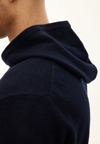 Granatowy hoodie o miękkiej strukturze, z luźnym krojem i wyraźnym kapturem, z detalem szwu na ramieniu.