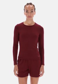 Cămașă bordó cu mânecă lungă, guler rotund și croială ajustată, asociată cu pantaloni scurți asortați. Textură netedă cu un branding subtil pe margine.