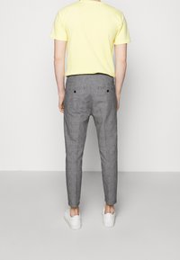 Szare spodnie w kratę, zwężane, z dwoma tylnymi kieszeniami i czarnymi guzikami. Noszone z żółtą koszulką z krótkim rękawem i białymi trampkami.