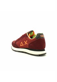 Sneaker in suede rosso con accenti neri, dettaglio grafico arancione e suola intermedia bianca. Presenta un colletto imbottito e una fodera interna colorata.