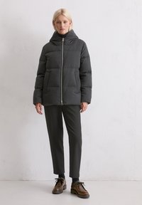 Szary puchowy kurtka z kapturem, z zamkiem błyskawicznym z przodu, dwiema dużymi kieszeniami z przodu i prostopadłym krojem. Nosi się ją z ciemnymi spodniami i butami.