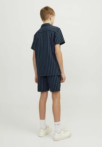 Chemise à manches courtes bleu marine avec des rayures blanches, assortie à un short. Le modèle porte des baskets blanches et des chaussettes blanches jusqu'aux chevilles.