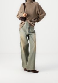 Maglione beige a collo alto, vestibilità rilassata. Jeans a gamba larga blu chiaro con finish sbiadito. Stivaletti marroni alla caviglia, abbinati a una borsa scura.