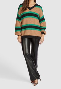Pull en tricot épais aux rayures beige, noir et vert ; encolure en V, poignets côtelés ; associé à un pantalon en cuir noir brillant et des talons ouverts.