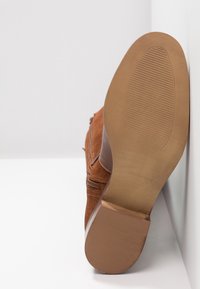 Bottine en daim marron vue de la semelle latérale, dotée d'une semelle extérieure en caoutchouc texturé et d'une fermeture éclair sur le côté intérieur.