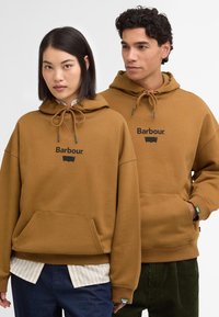 Καφέ φούτερ με κουκούλα και κορδόνι, μπροστινή τσέπη και λογότυπο Barbour, φορεμένο πάνω από πουκάμισο λευκού και μπλε ριγέ σχεδίου, παρουσιασμένο σε δύο μοντέλα.