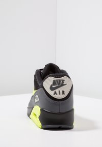 Černá a šedá teniska s texturovaným koženým a síťovaným svrškem, zářivě žlutými akcenty a výraznou šedou patní sponou s nápisem "Nike Air".