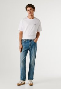 Valge lühikeste varrukatega t-särk, millel on väike logo, koos helesiniste otsejoonistega teksade ja lihtsate valgete sneakeritega, millel on beeži tooni aktsendid.