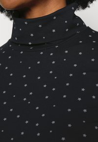 Tmavě modrý rolák z měkké látky s rozptýlenými šedými hvězdami. Límec je vysoký a těsný, s hladkou texturou.