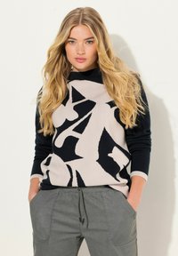 Suéter de punto con patrón abstracto en negro y beige, cuello alto y mangas ajustadas, combinado con pantalones casuales grises.