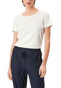 Weißes Baumwoll-T-Shirt mit kurzen Ärmeln, rundem Ausschnitt und lockerer Passform. Kombiniert mit marineblauen Jogginghosen mit Reißverschlusstaschen und Kordelzug.
