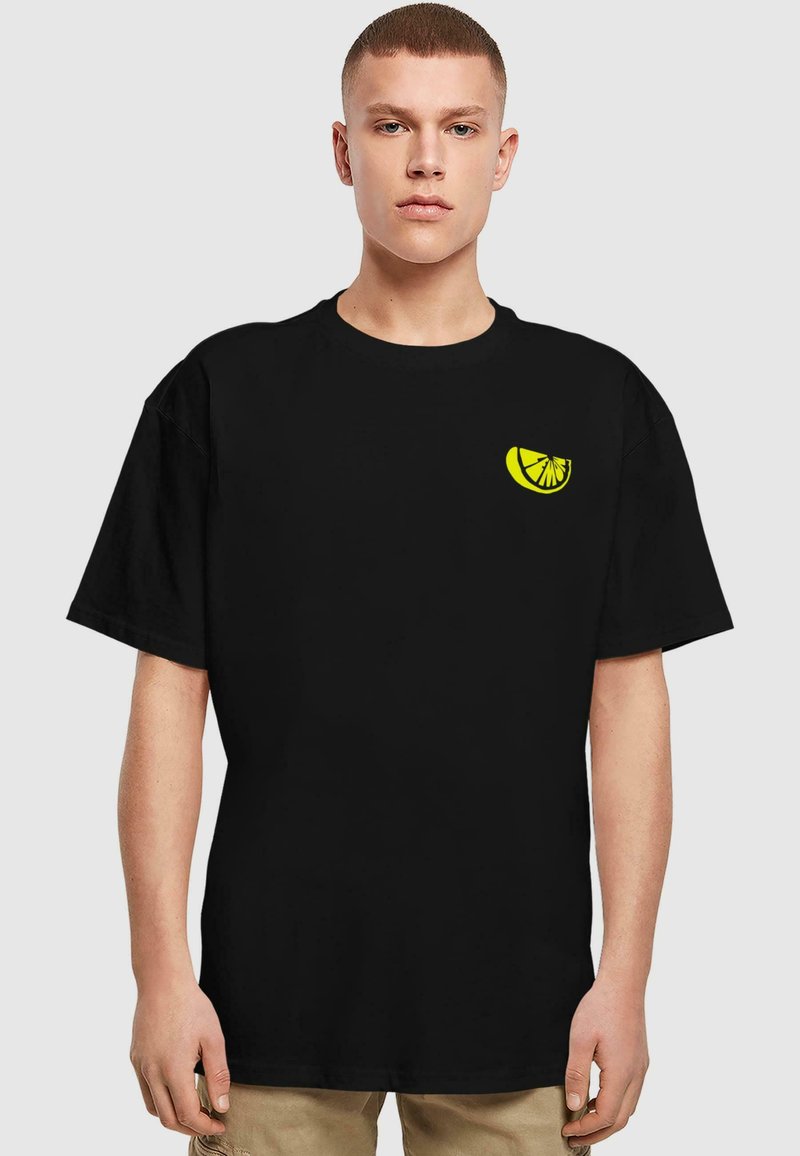 T-shirt en coton noir avec un petit graphique de rondelle de citron jaune sur la partie gauche de la poitrine, à manches courtes et à coupe décontractée.