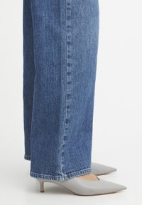 Tacones de piel gris con puntera afilada y tacón bajo, combinados con jeans de mezclilla rectos de un oscuro azul que presentan un diseño clásico de cinco bolsillos.