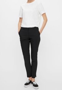 Svarta skräddarsydda byxor med slim fit, slätt tyg och sidofickor. Matchas med en vit skjorta med kort ärm och svarta sneakers.