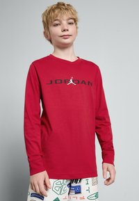 Rød langermet skjorte laget av myk tekstil, med svart "JORDAN"-logo og Jumpman-grafikk. Enkel, rett snittdesign.
