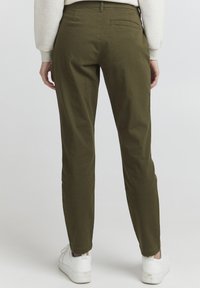 Olive green chinos with a slim fit, featuring a back pocket and a smooth texture, paired with white sneakers.