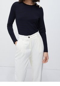 Granatowa bluzka z długim rękawem w paseczki, z prążkowaną fakturą, z ozdobnym złotym guzikiem na ramieniu, zestawiona z białymi, fakturowanymi spodniami o wysokim stanie.