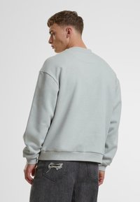 Hellgraues Sweatshirt mit Rundhalsausschnitt und langen Ärmeln. Hat eine glatte Textur und gerippte Bündchen. Kombiniert mit dunkelgrauen, abgetragenen Jeans.