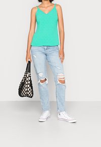 Mintgrön strukturerad linne, ljusblå slitna jeans, vita sneakers och en svart meshtote.