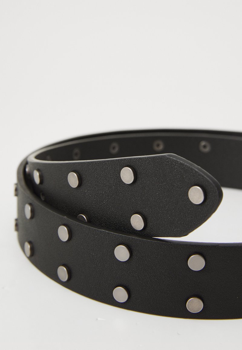 Cinturón de cuero negro con un acabado texturizado, que presenta tachuelas de metal plateado distribuidas uniformemente a lo largo de su longitud y una punta afilada.